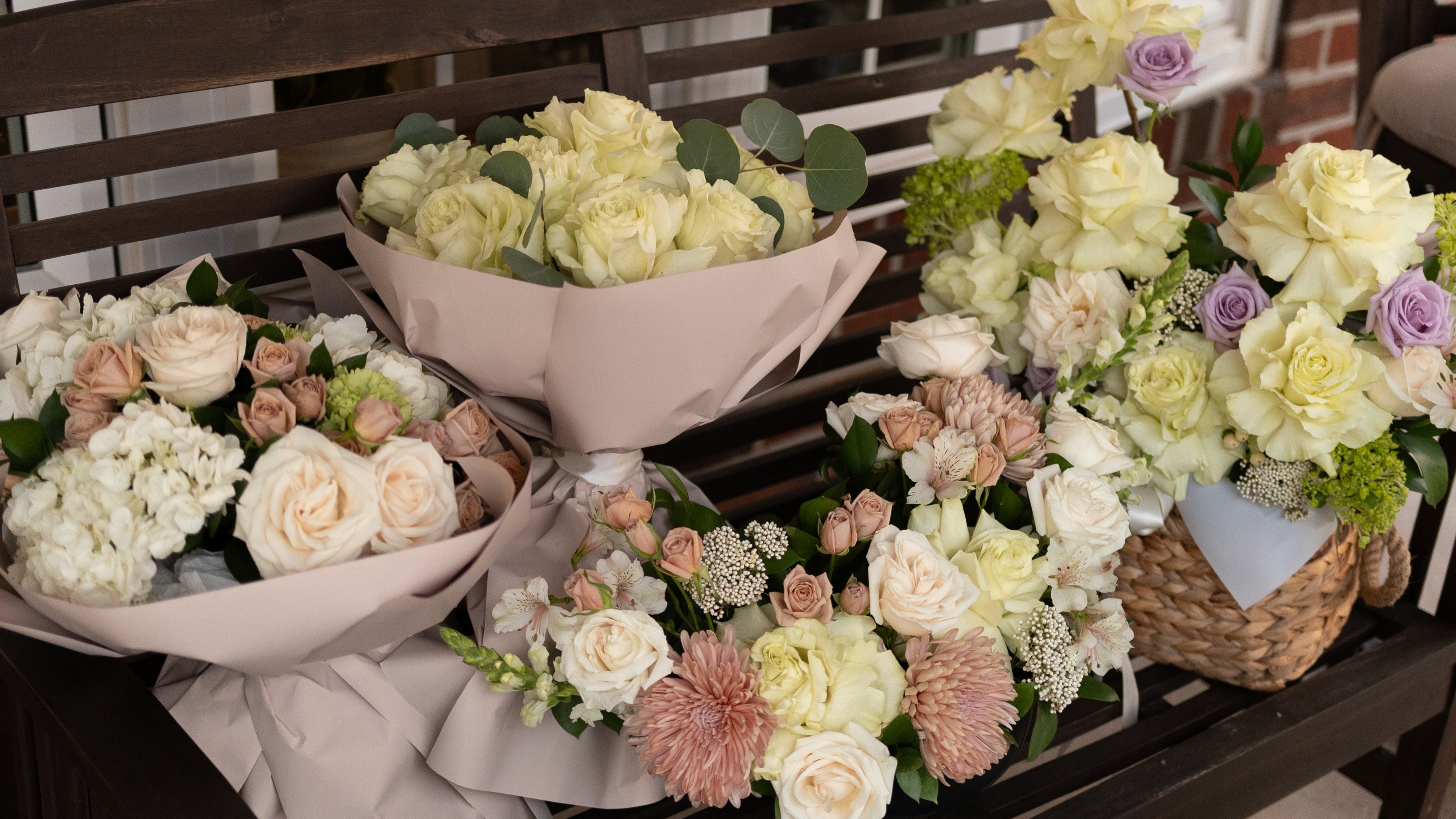 Bouquets of flowers arranged on a wooden bench outdoors.